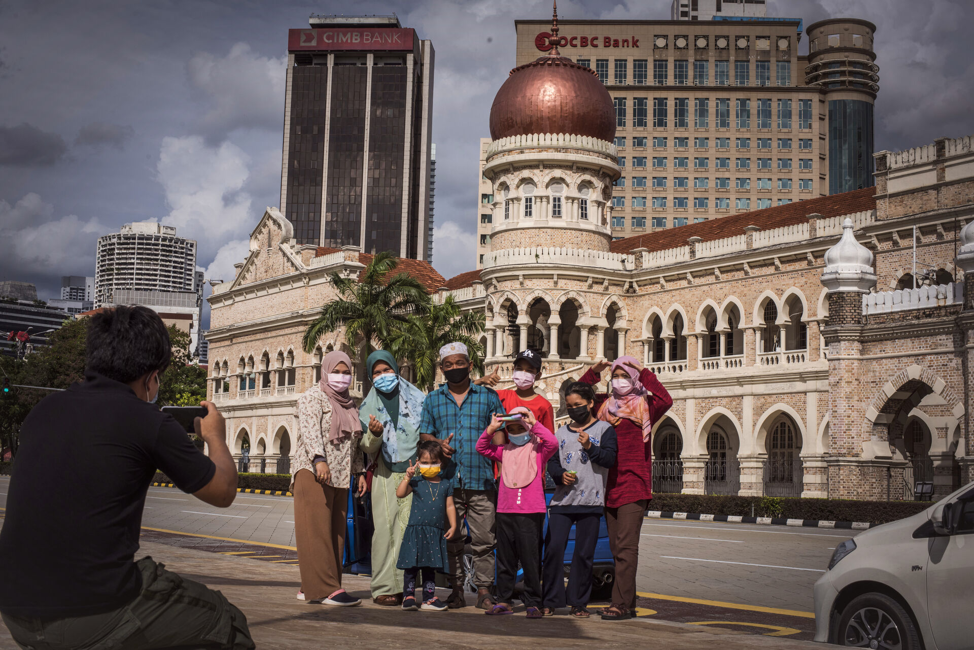 Group posing for a photo in front of a historic domed building, wearing face masks, as a photographer takes the picture.