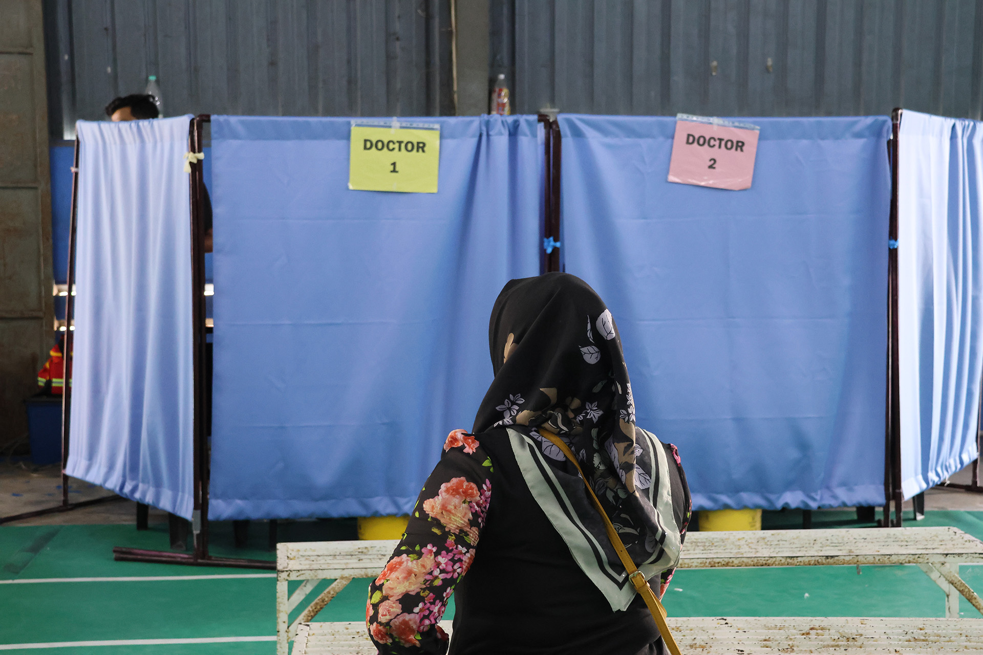 A person in a floral headscarf is n front of two medical booths labeled 