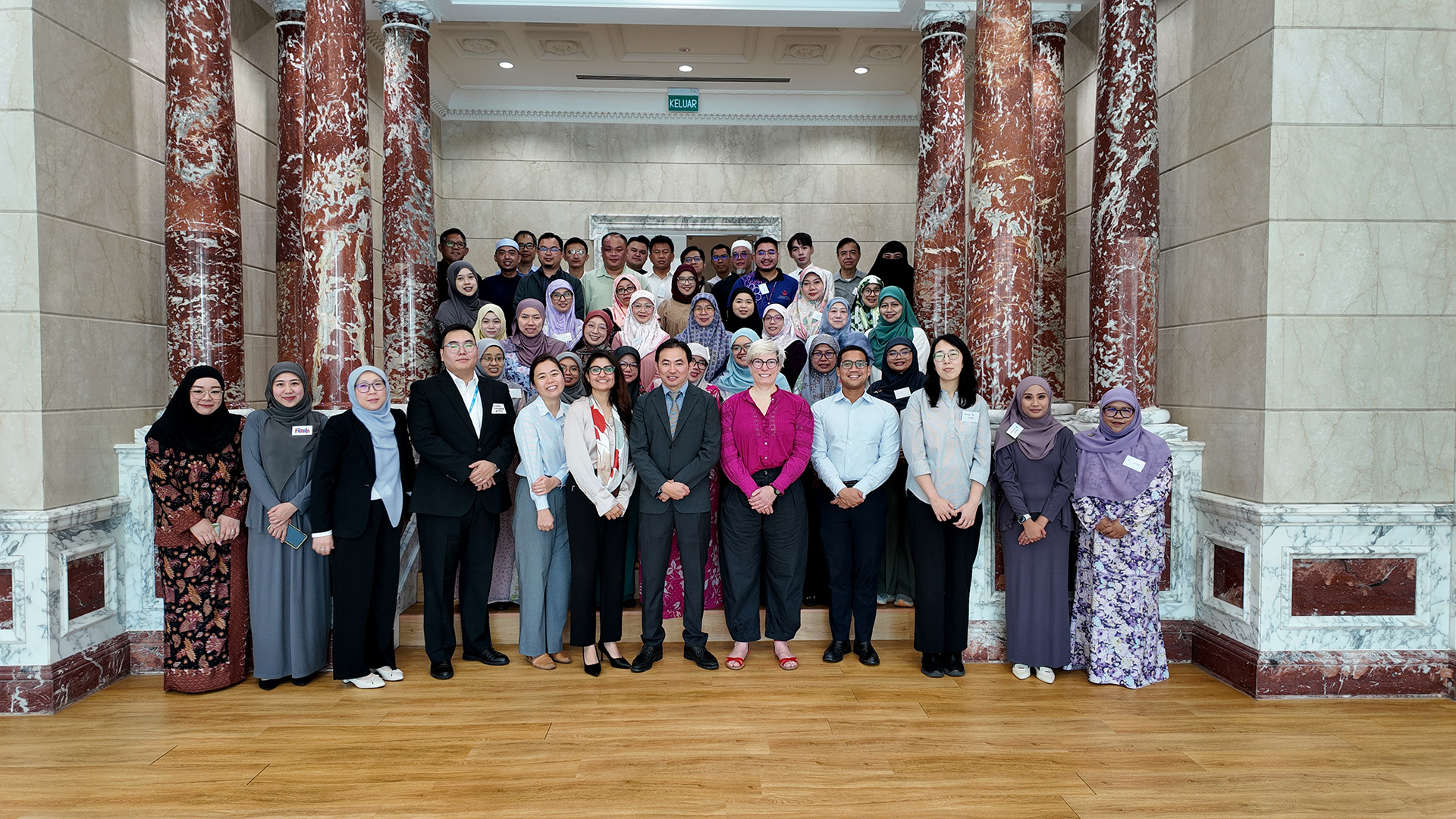 Group photo of training participants standing in a hall with marble columns.