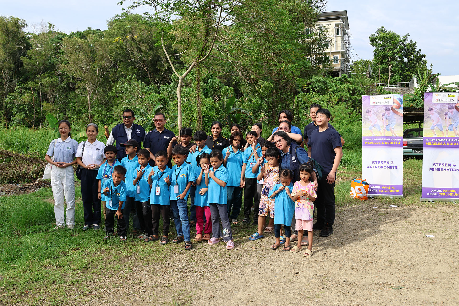 Children and adults in blue shirts pose outdoors near banners during a community health awareness event.