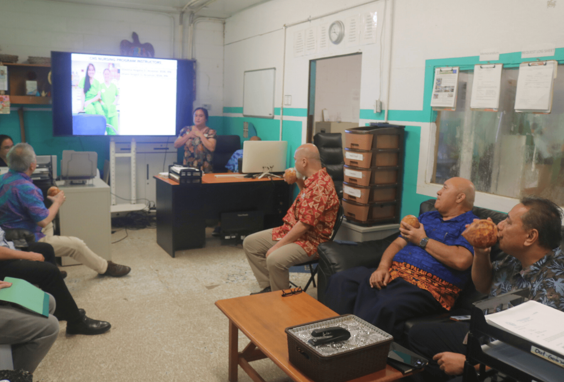 A group of people listens to a presenter in front of a screen