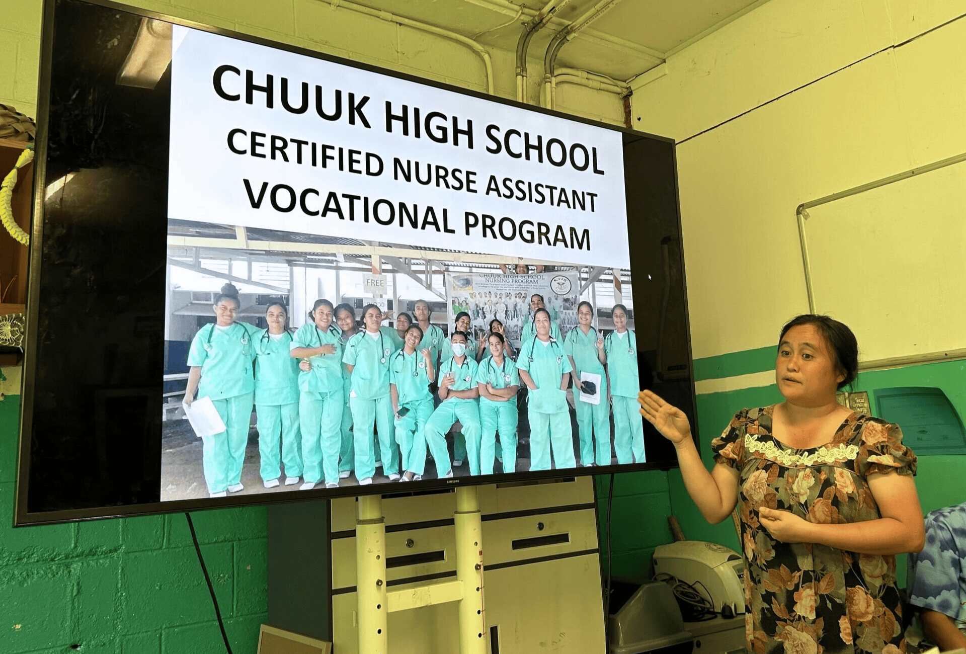 A group of people listens to a presenter in front of a screen
