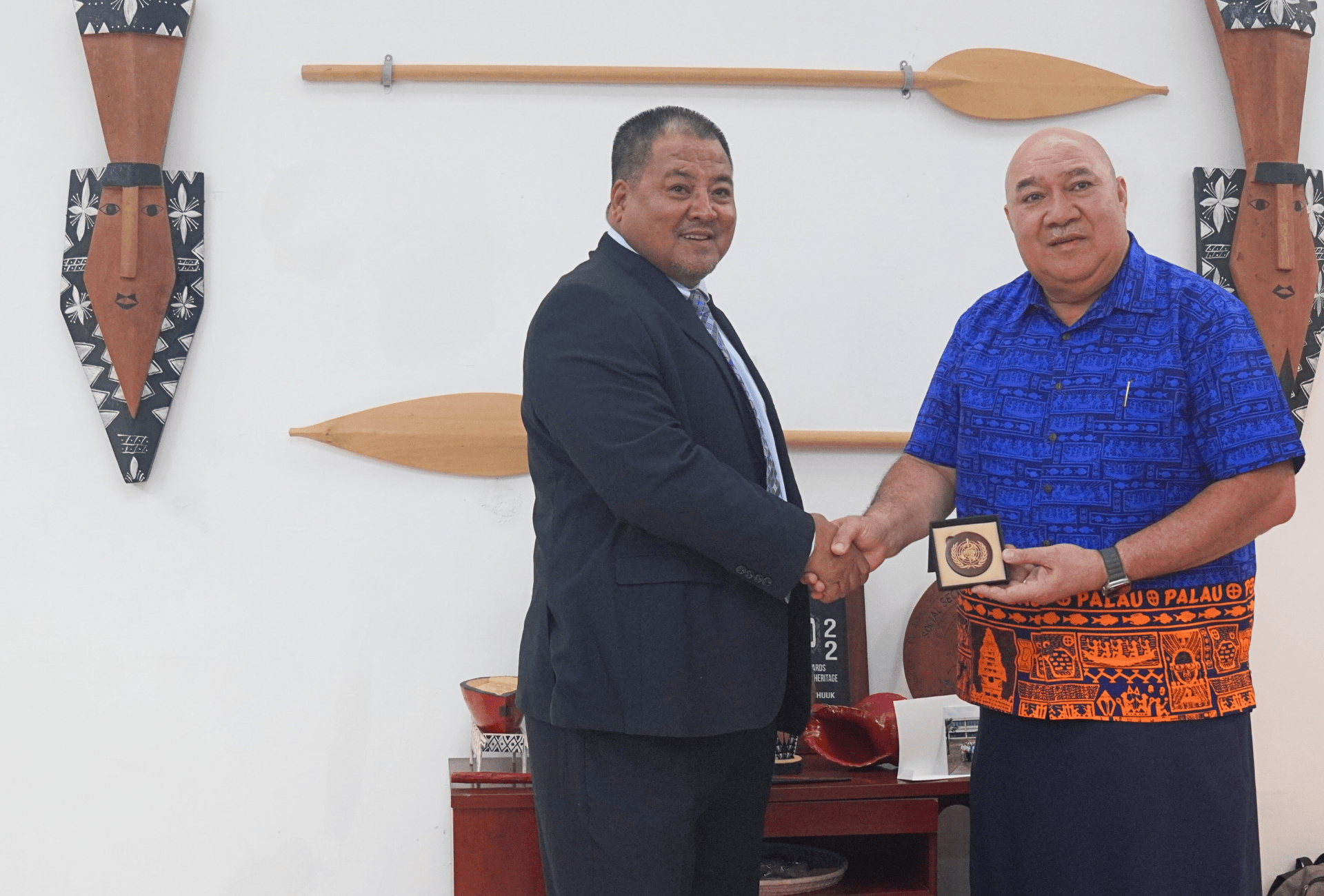 Two people shaking hands; wall behind them displays wood crafts