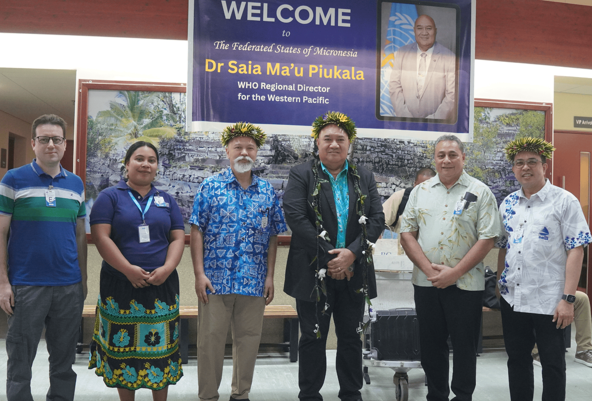 A group photo in Micronesia with a welcome banner for Dr Saia Ma'u Piukala behind them