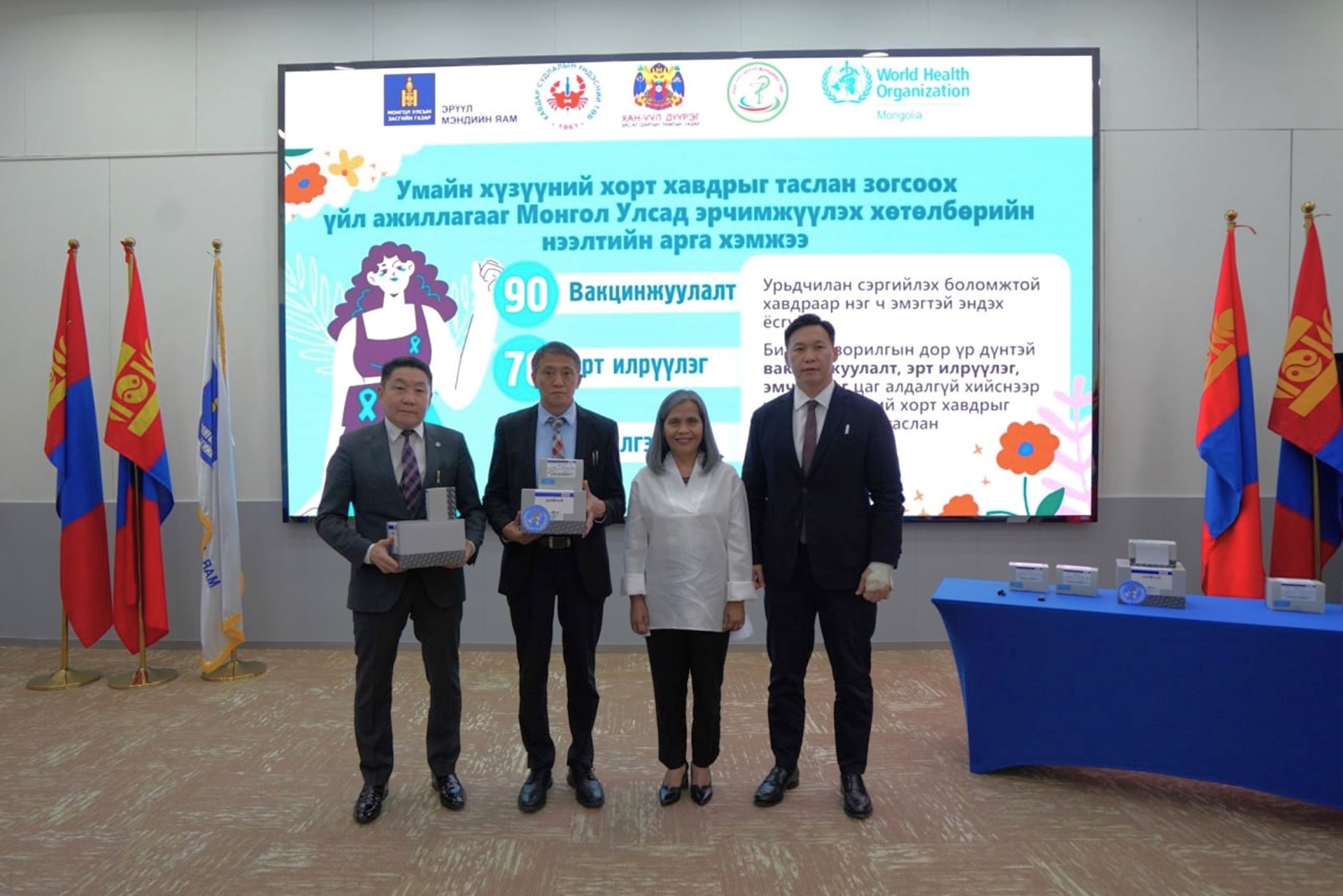 A group of people in front of a LED screen that contains text in Mongolian