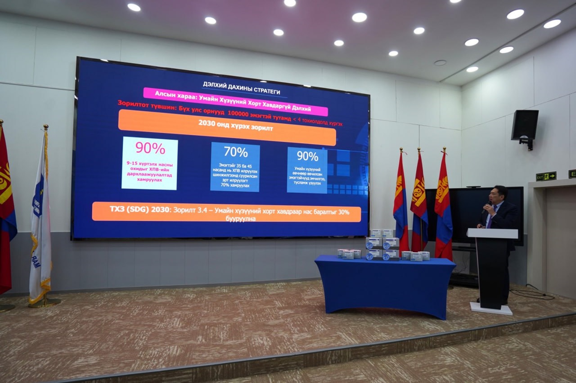 A presentation in Mongolian shown on a stage screen, with the speaker on a podium on the right side
