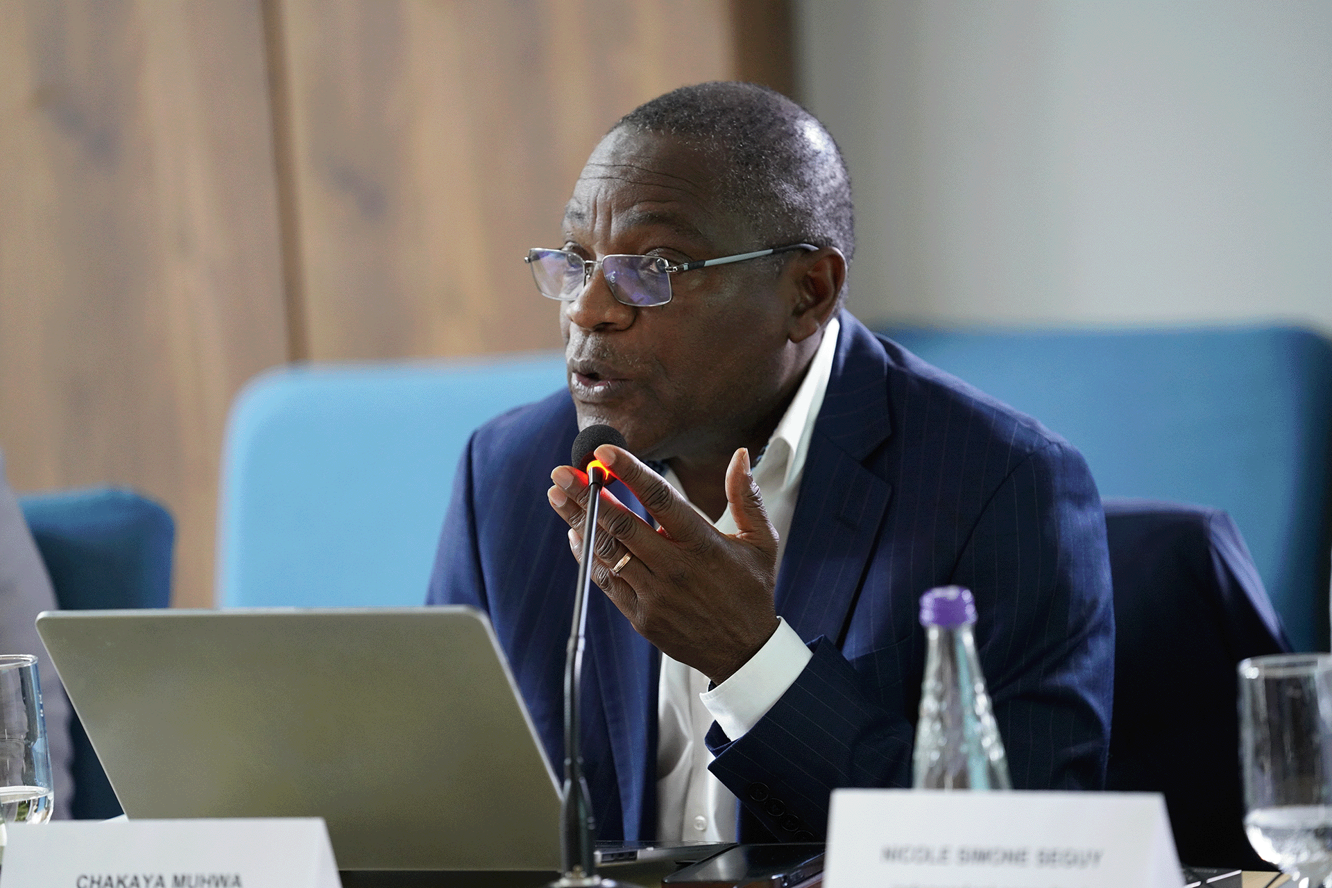 Speaker seated at a conference table, speaking into a microphone during a tuberculosis programme review meeting