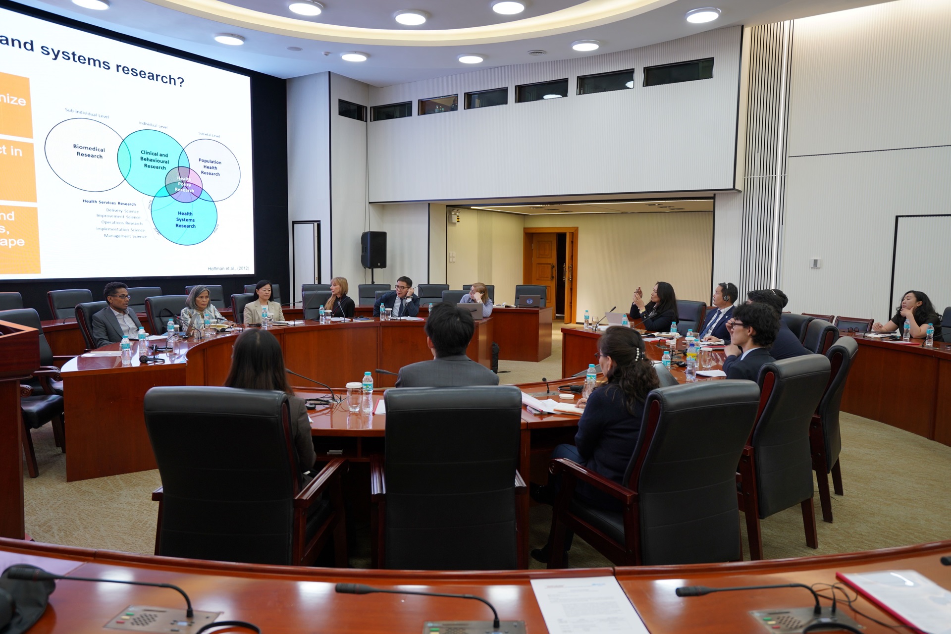 Group meeting around a conference table viewing a slide on health systems research.