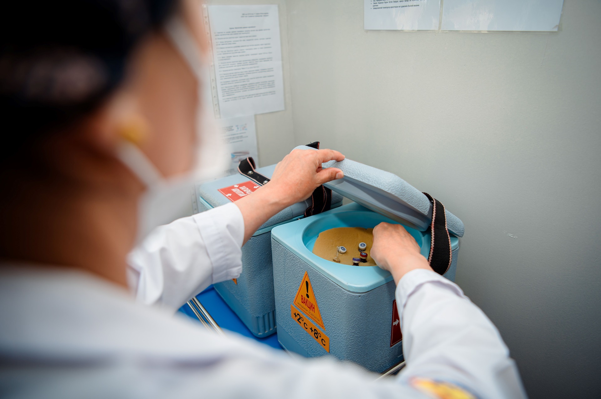 Health worker opens a vaccine cold box labeled “2°C to 8°C,” checking vials stored inside during immunization work in Mongolia.