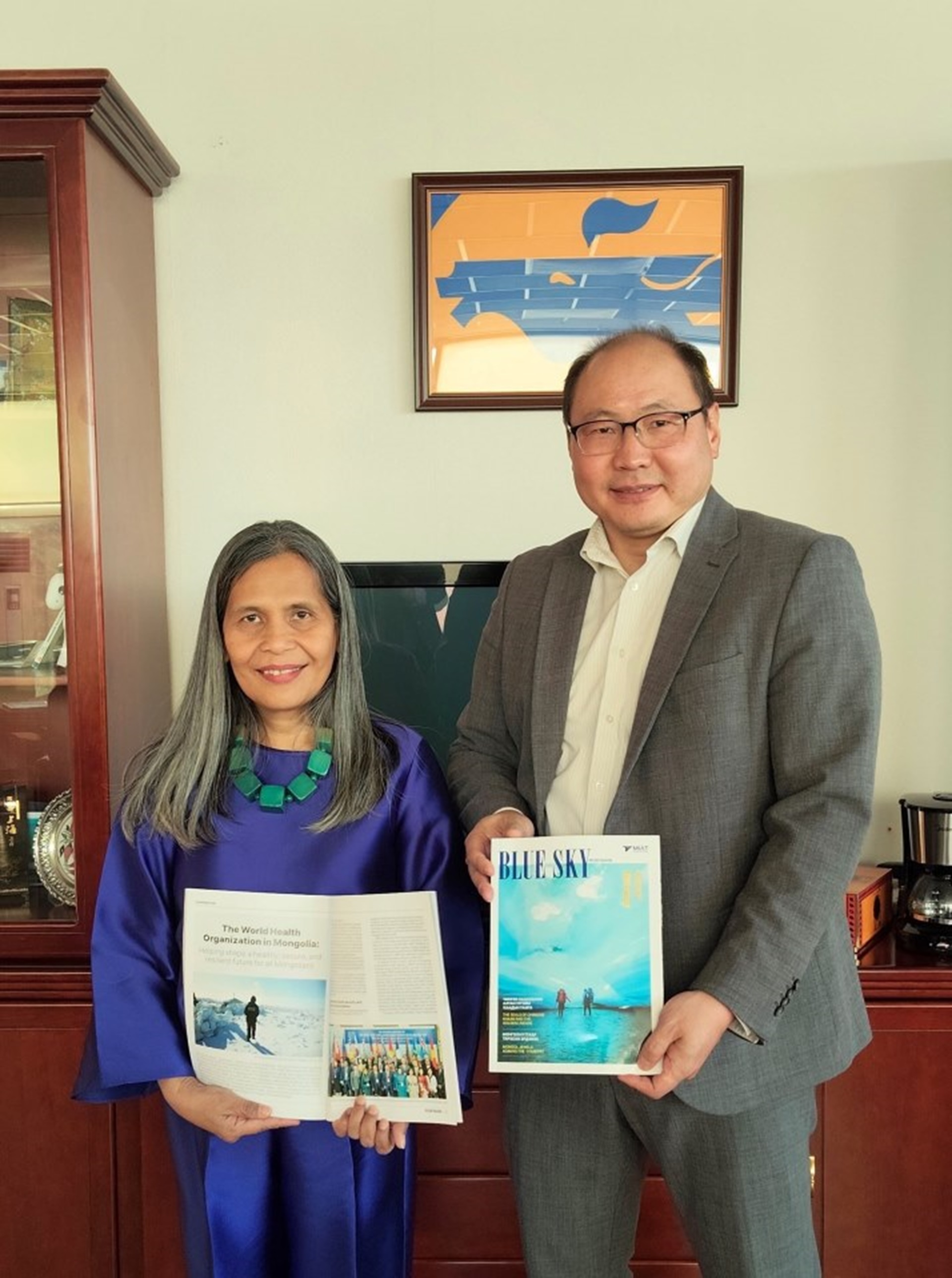 A man and a woman holding a magazine and smiling to the camera