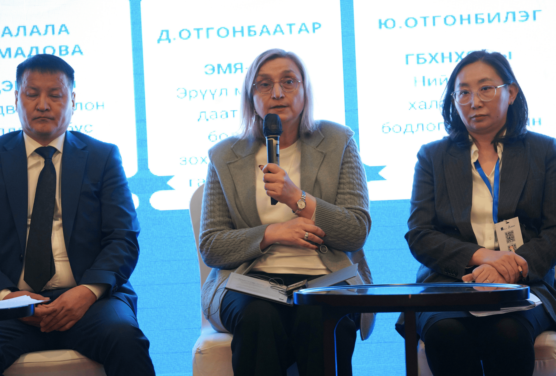 Two women and a man sit on a stage