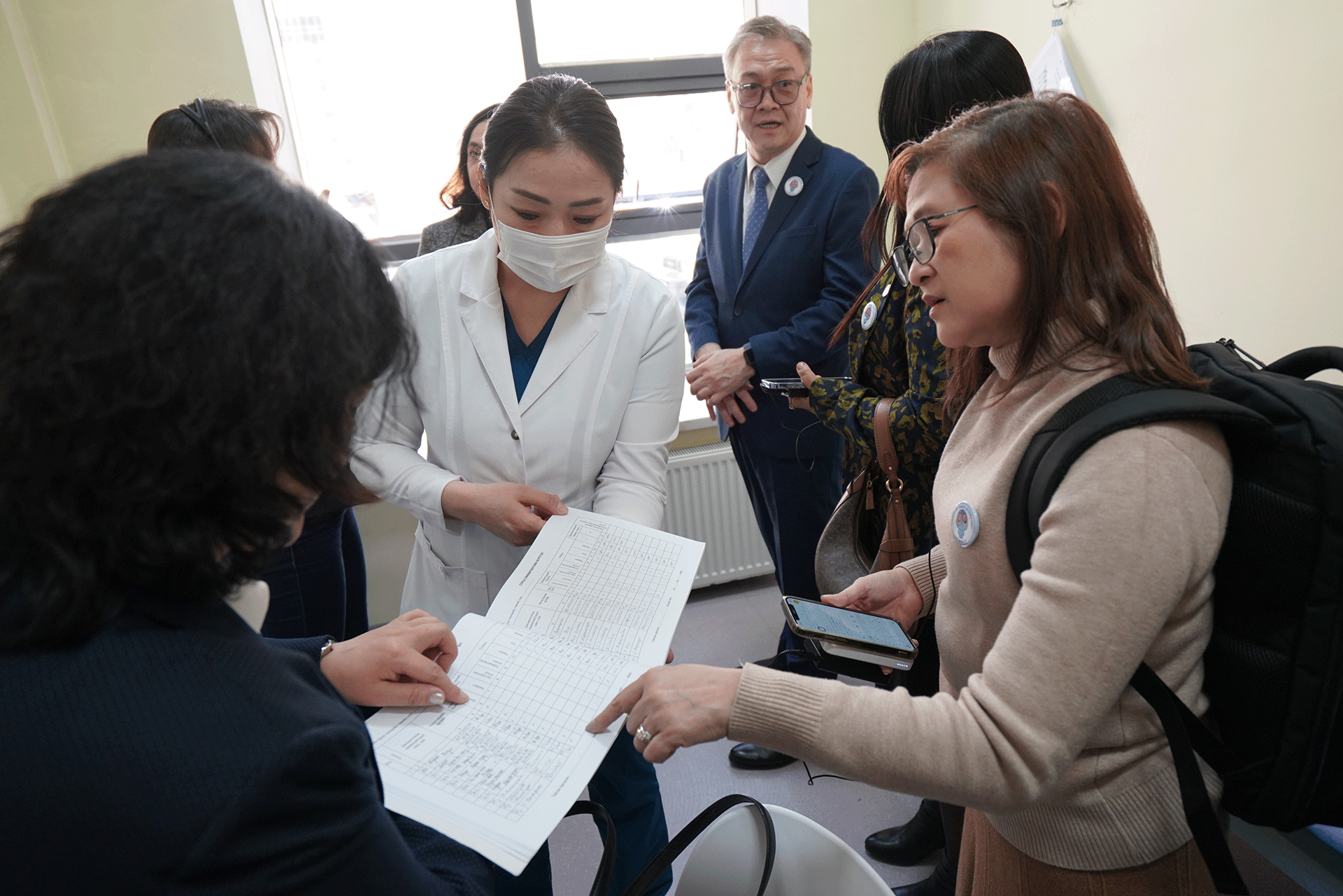 Health workers and reviewers standing together indoors, examining printed tuberculosis service data during an on-site review
