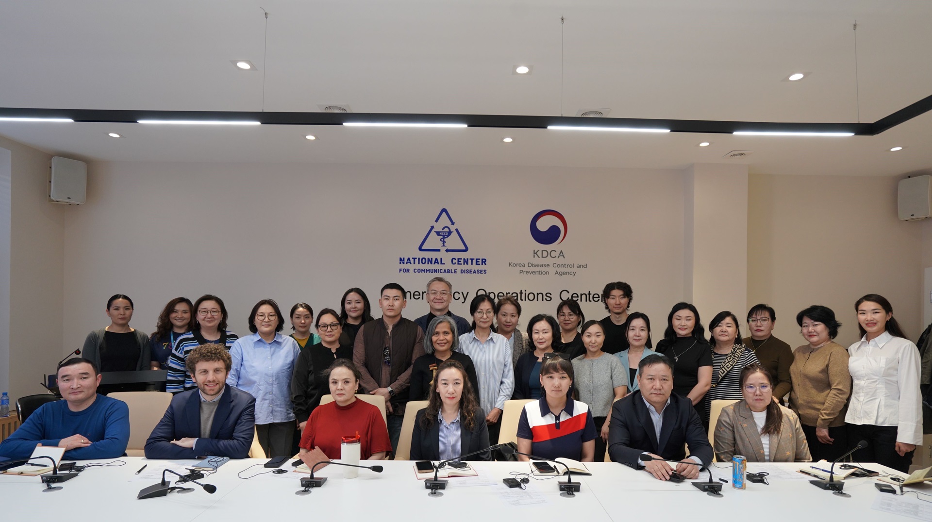 Group photo of people seated on a long table with people standing behind them