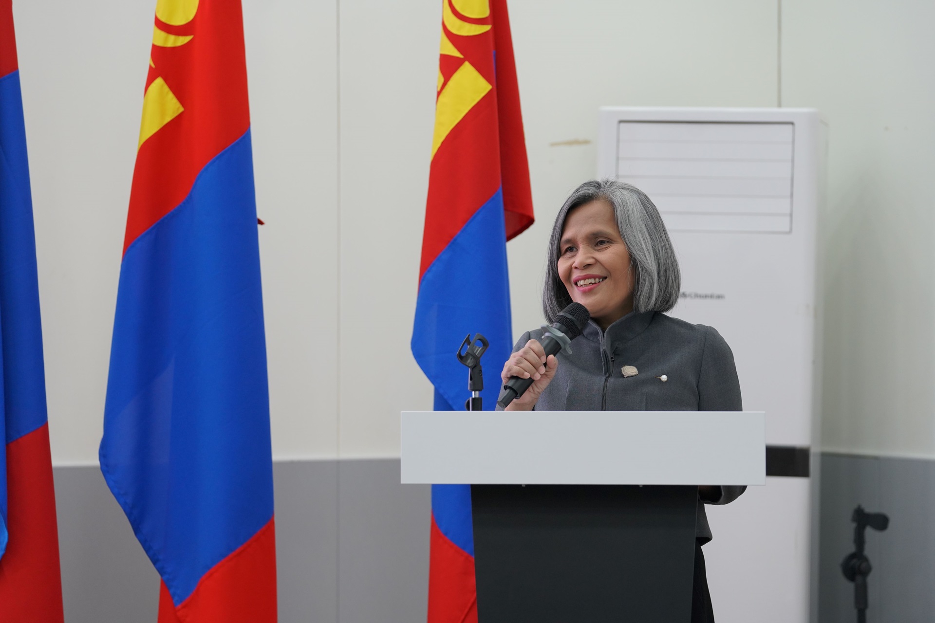 A woman speaks at a podium. Mongolia flags are in the background.