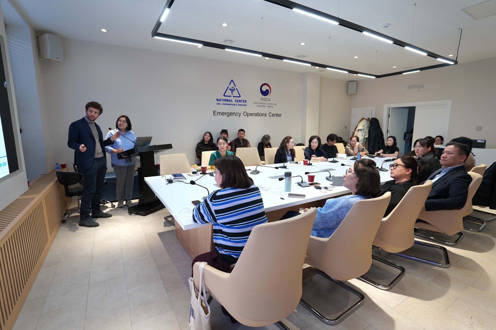 People seated around a rectangular table. Two people present in front.