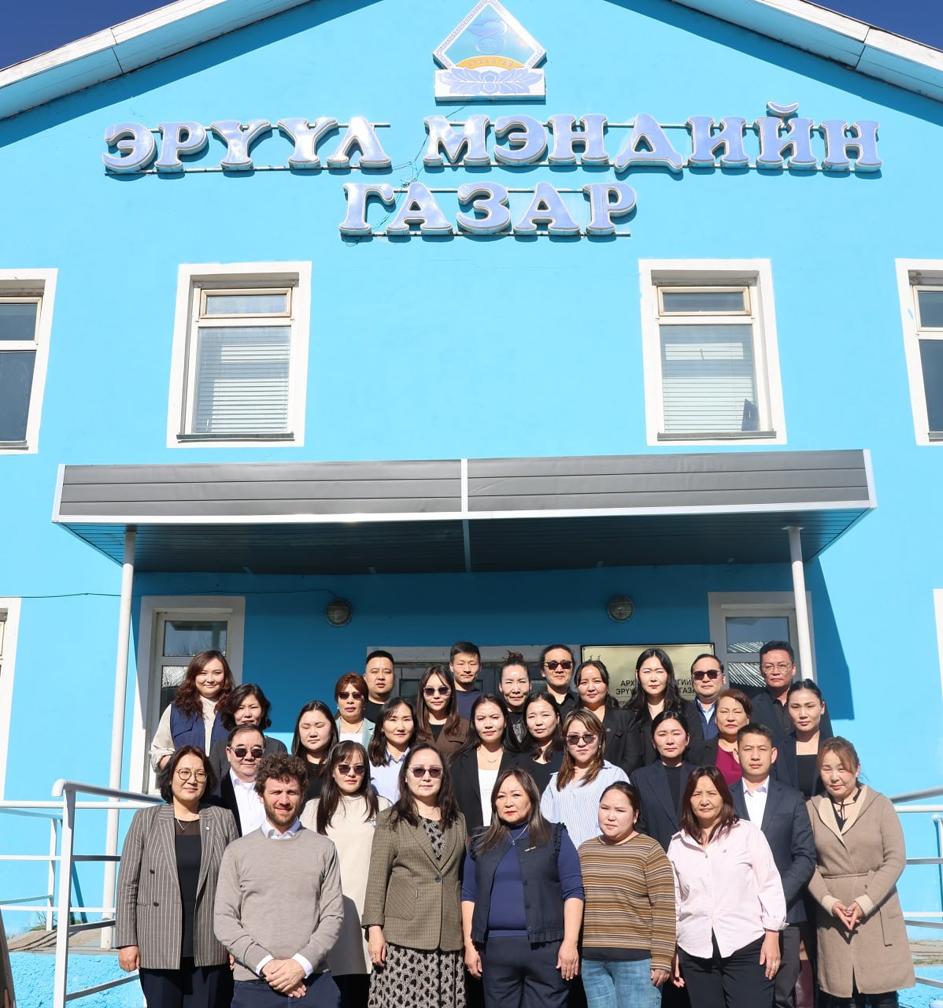 Group photo of people standing in front of a blue structure with Mongolian words on its facade.