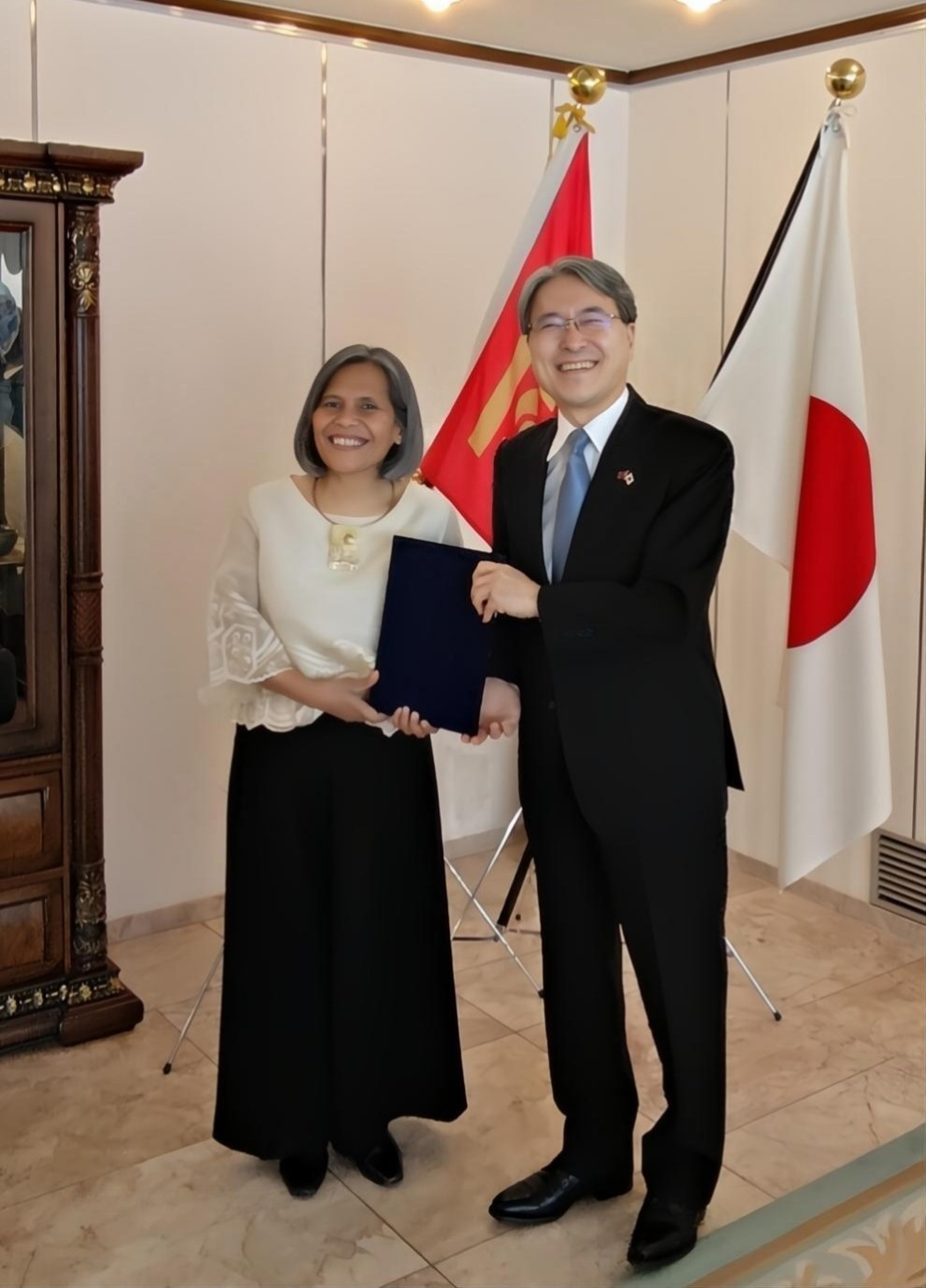 Two people holding a booklet of document between them. The flags of Mongolia and Japan are in the background.
