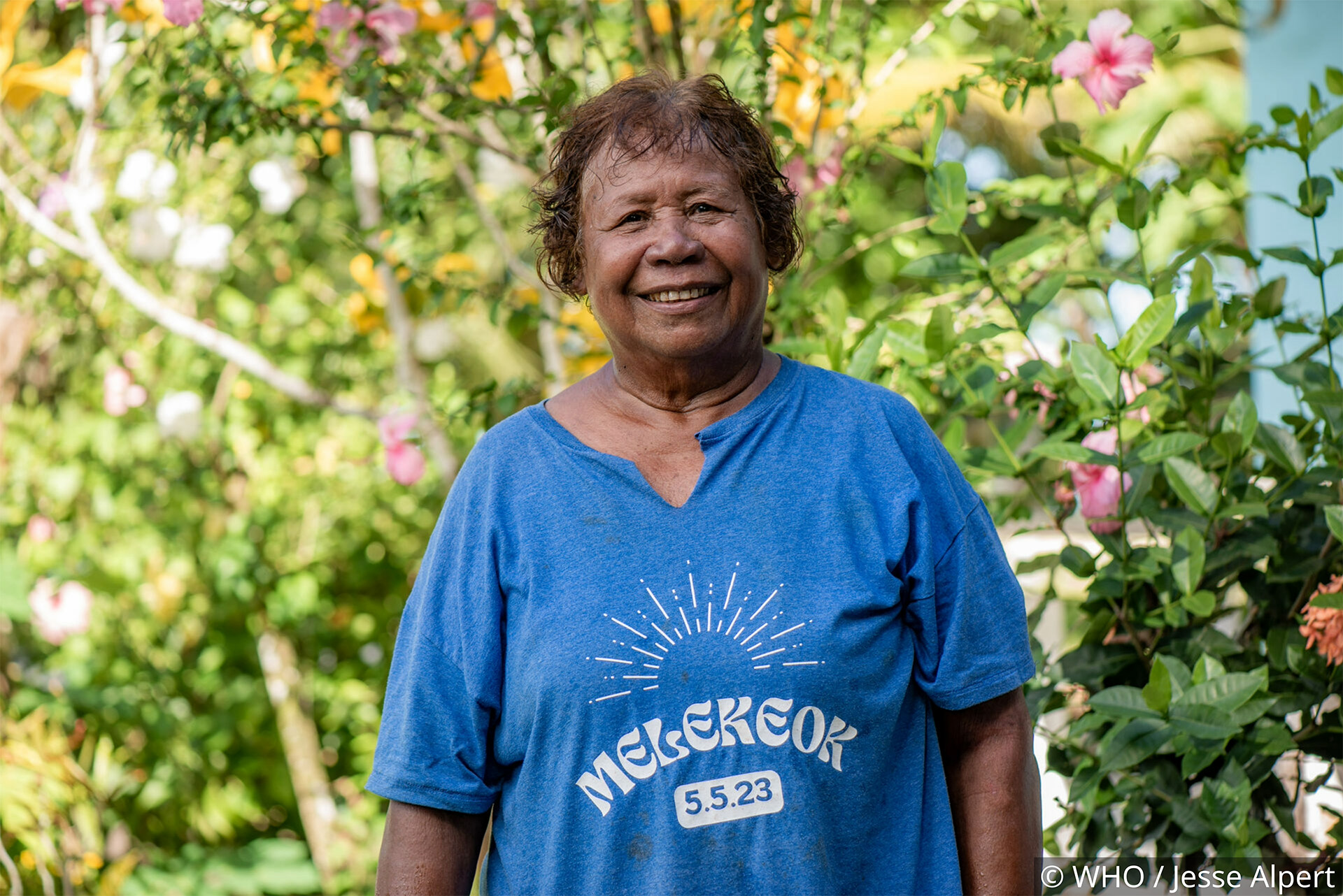 Person wearing a blue shirt standing in a garden with pink flowers and greenery.
