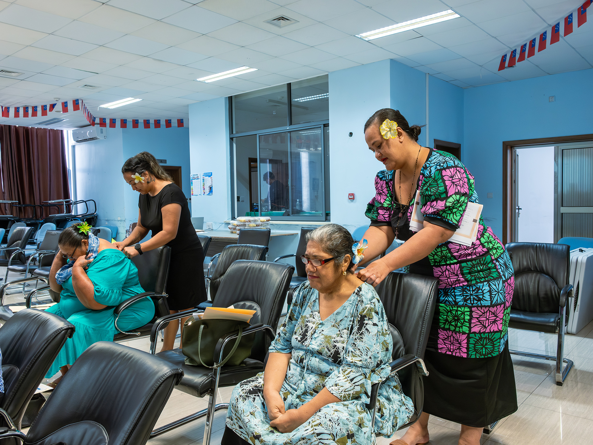 Community training in Vaitele on maternal care techniques as part of the First 1000 Days program, with two facilitators standing and demonstrating massage on seated participants.