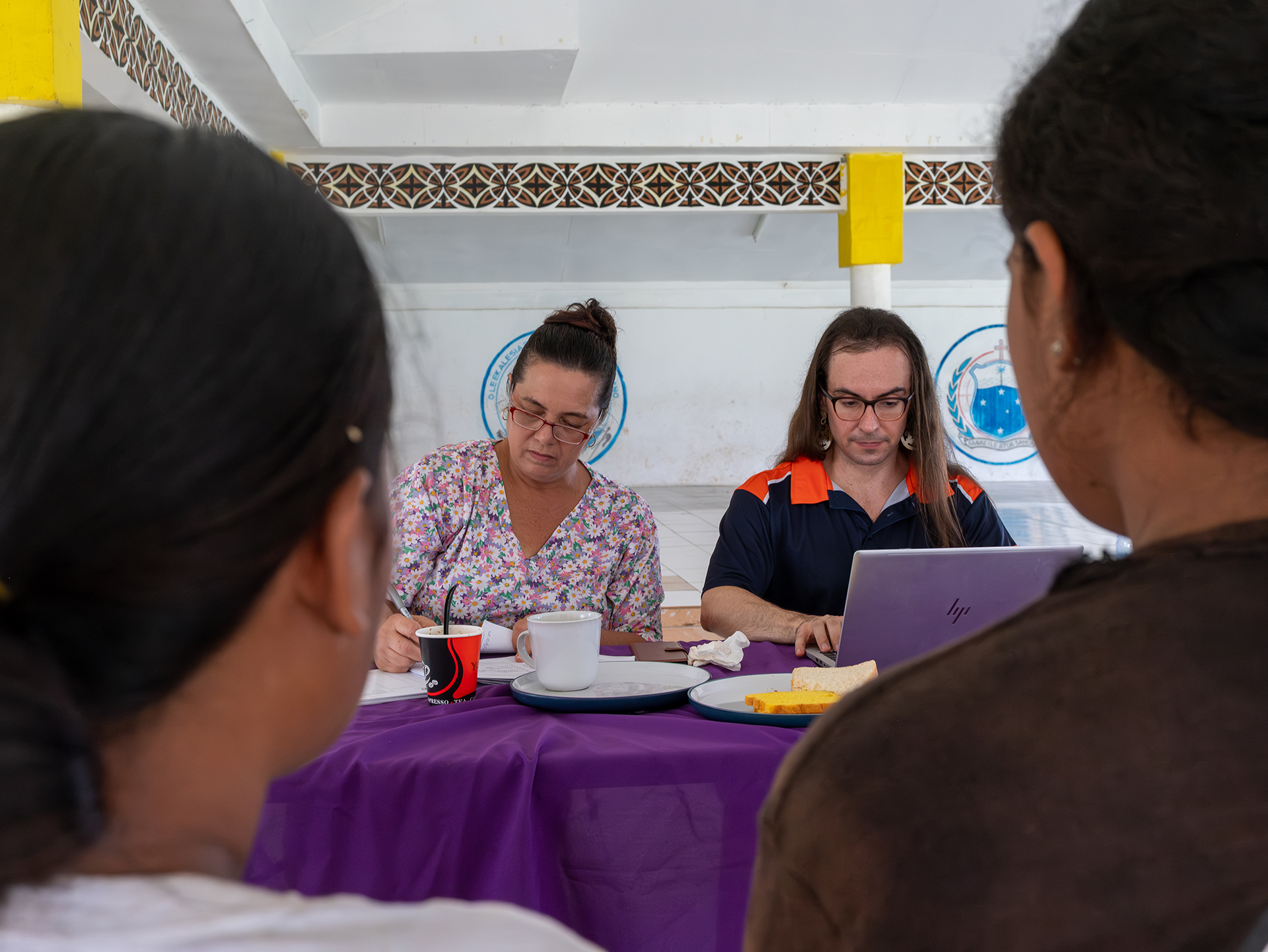 Two people sit at a table with a laptop and record books during an immunization outreach activity.