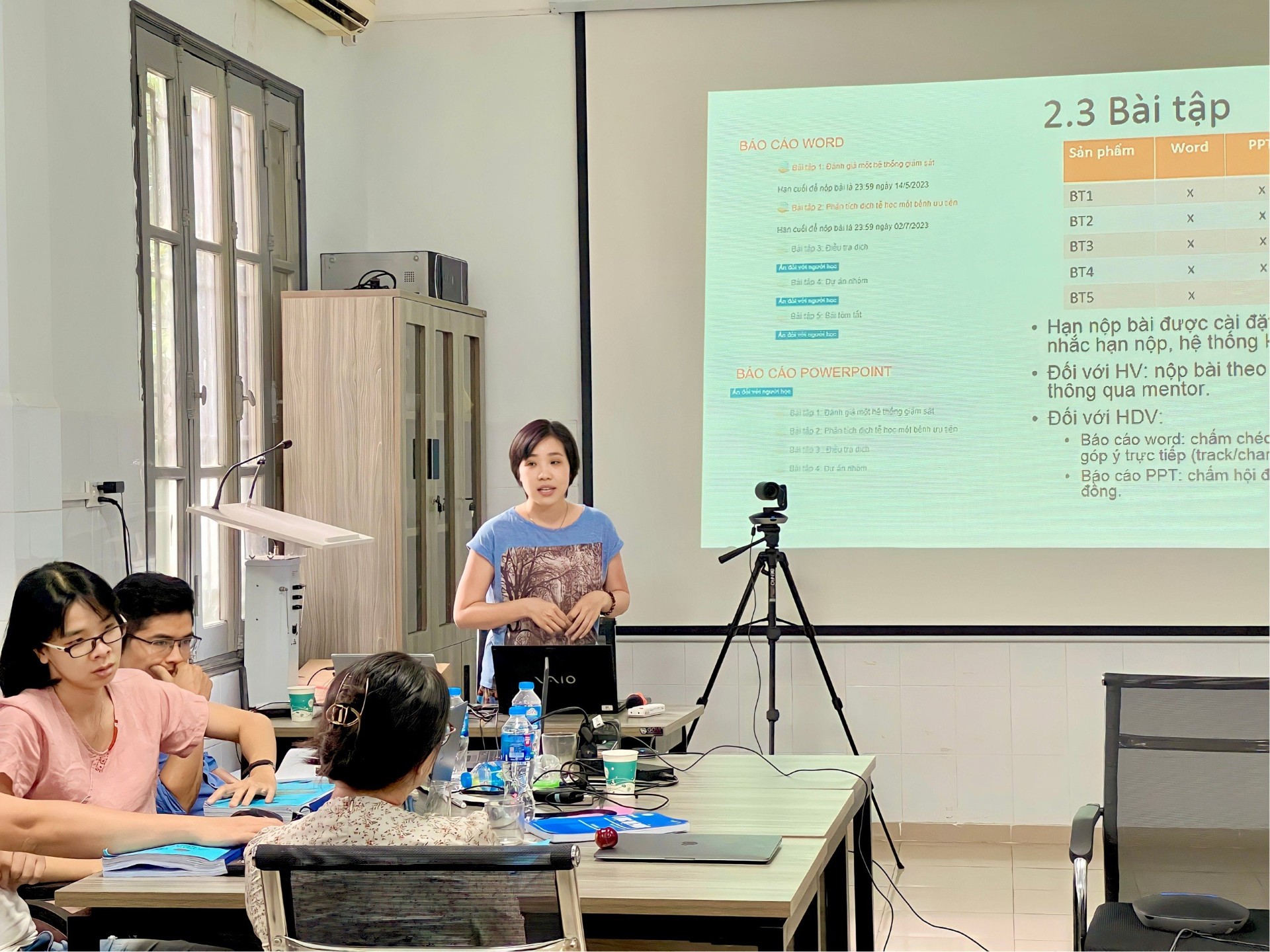 Woman presenting information to a group of three people who are sitting around a table.
