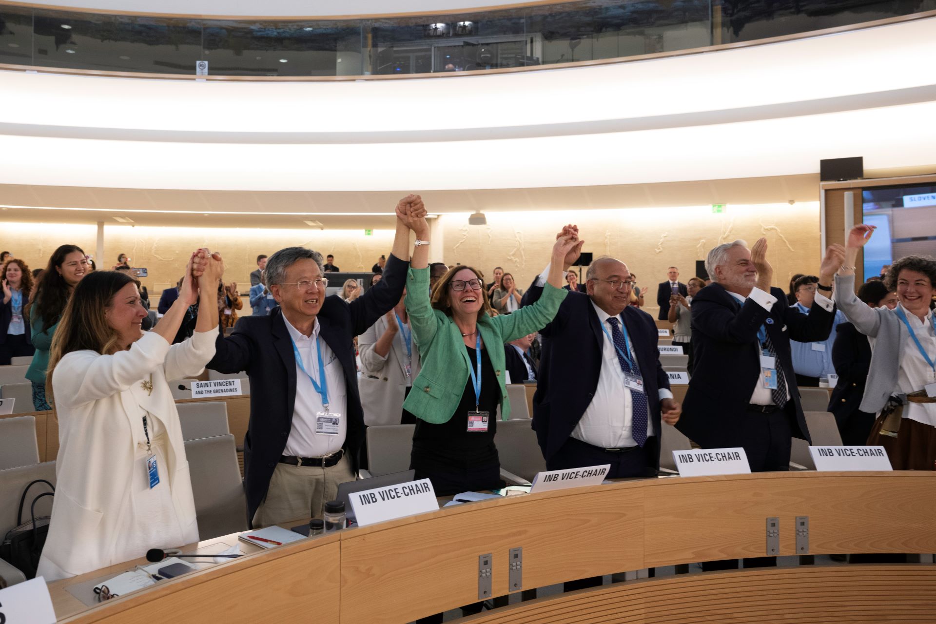 People in a meeting room joining their hands in the air and smiling