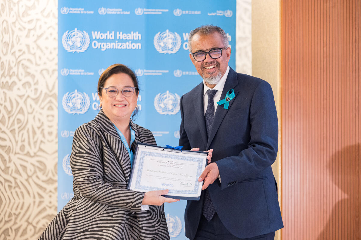 Smiling staff member of the WHO Regional Office for the Western Pacific receives certificate from the WHO Director-General. Both are smiling.