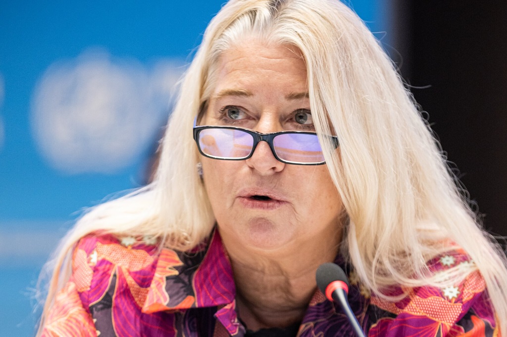 A woman wearing glasses speaking into a microphone.