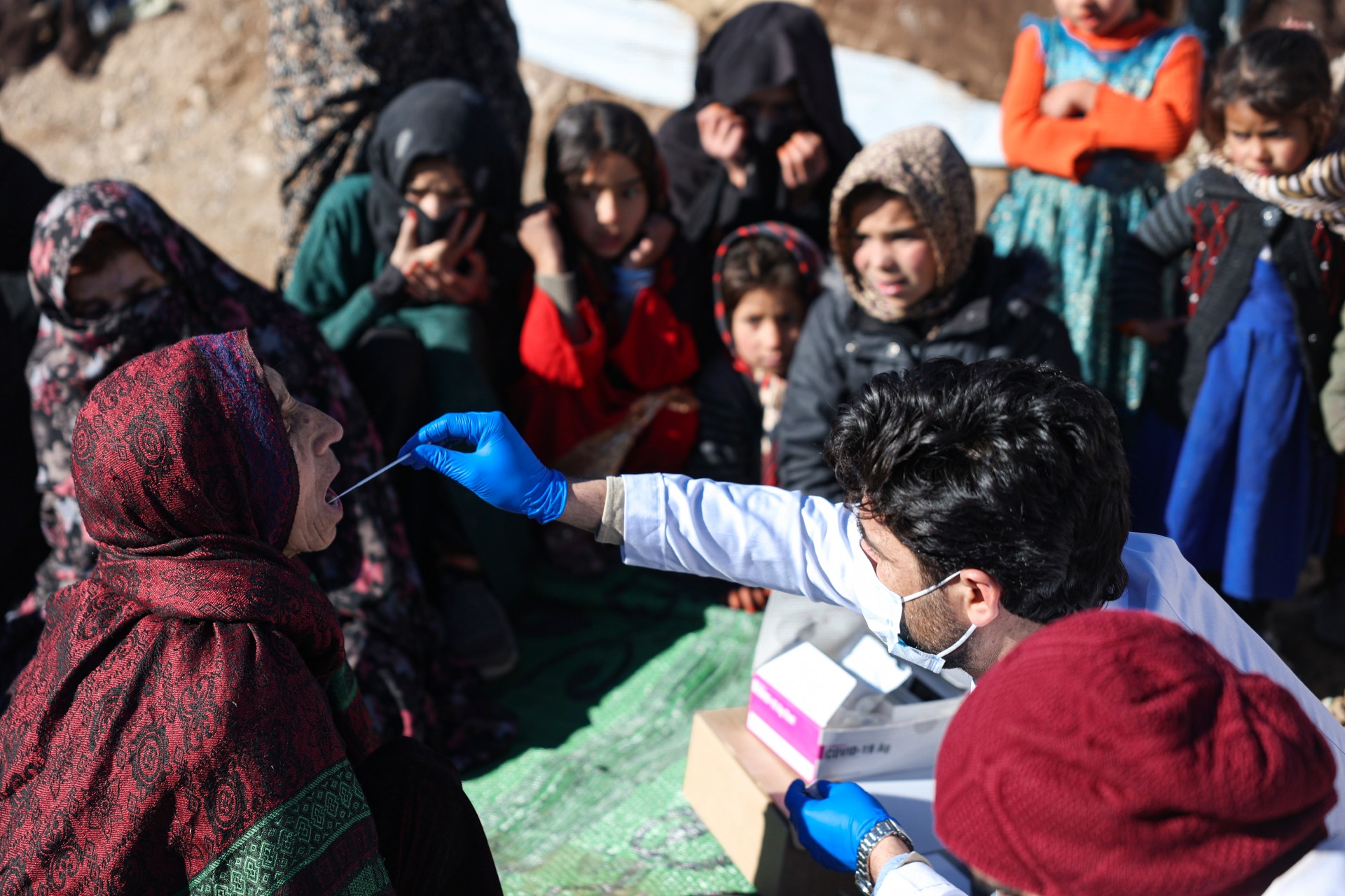 Health professional with a woman in the middle of a crowd of people in an outdoor location
