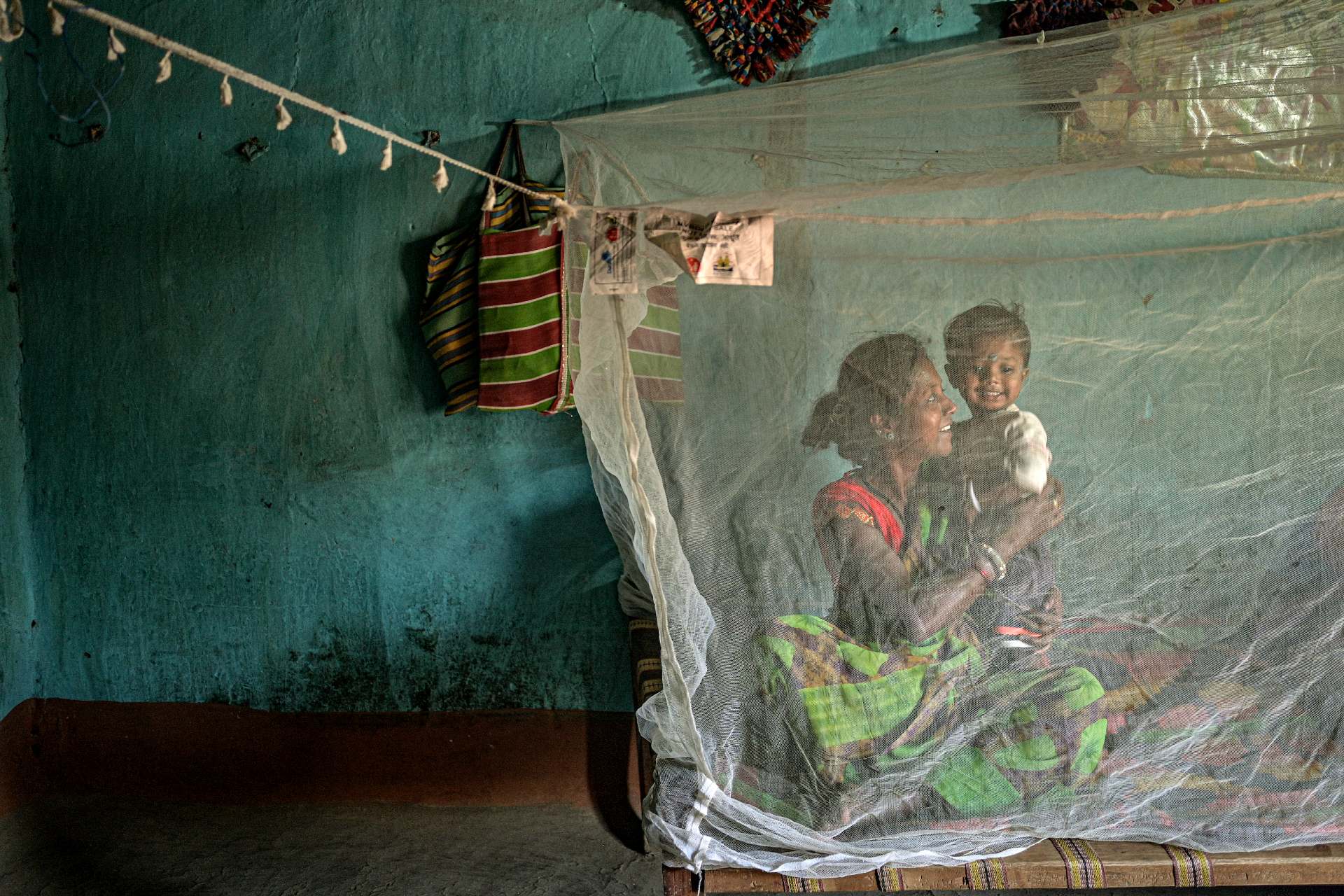 A smiling mother and child sit under a bed net.