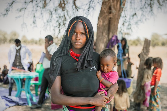 A mother is holding her 12-month baby on her hip, both looking into the camera