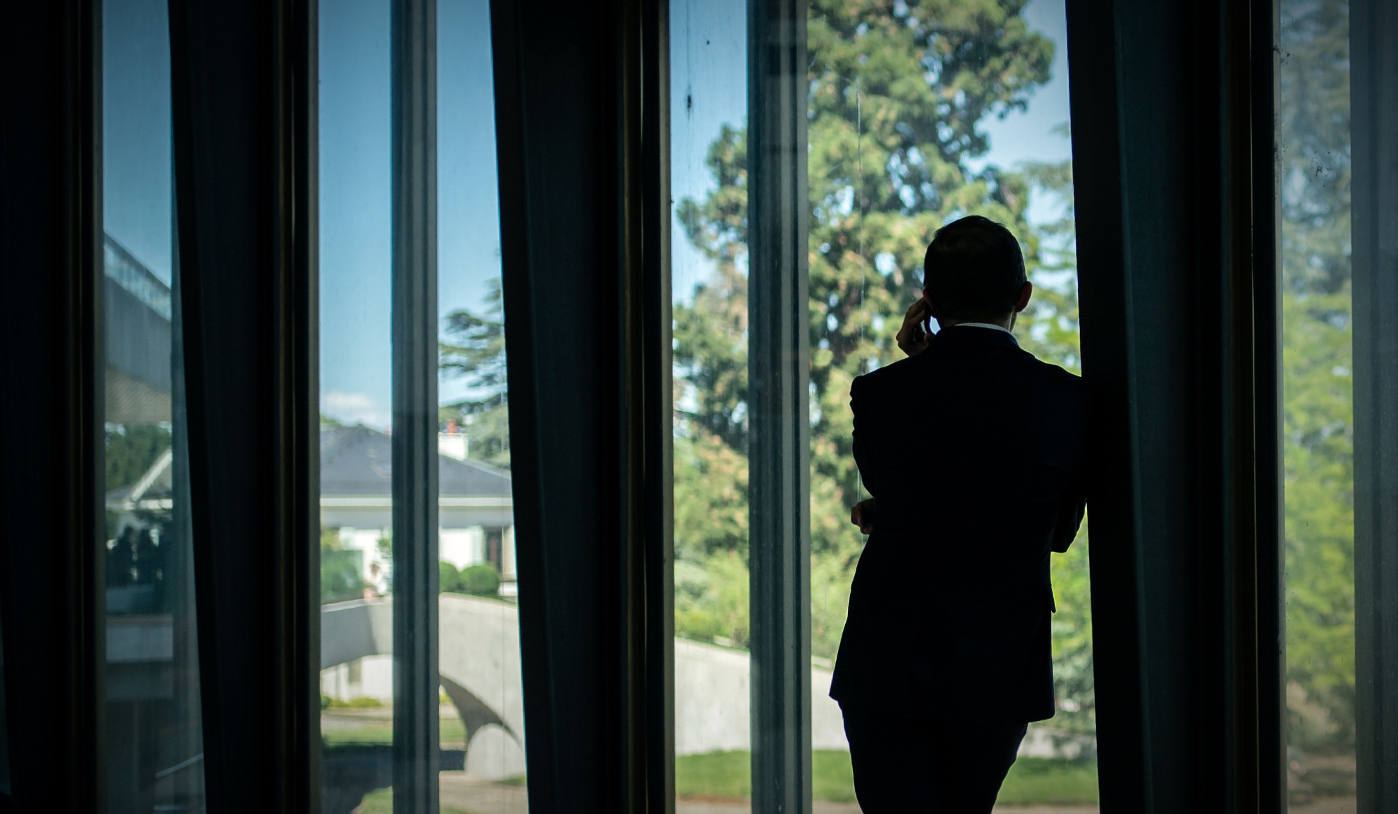 A silhouette of a man leaning against a pillar and talking on the phone, seen from behind and at a distance.