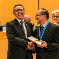 Two men are shaking hands and laughing during a prize ceremony.