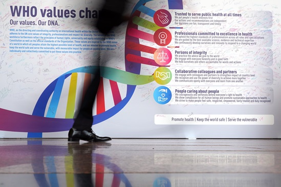 Photo of a wall display of WHO Values Charter, with the shadow of a person's legs walking by.