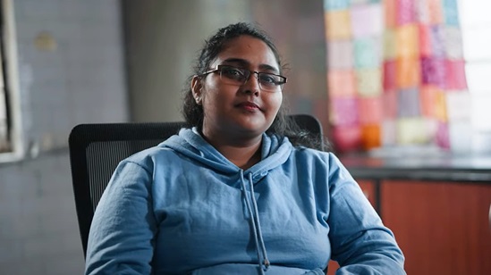 Video snapshot of woman sitting in a chair looking into the camera.