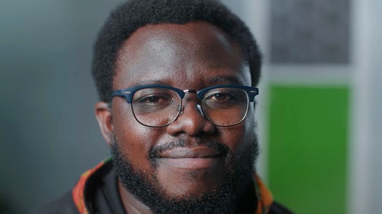 Video snapshot of the face of a man with glasses looking into the camera.