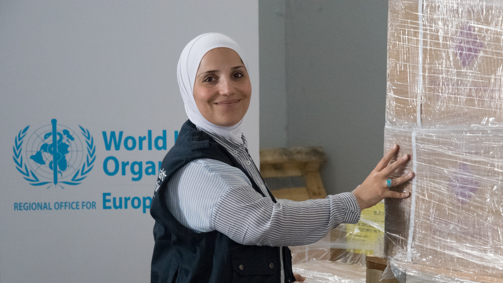 A woman  working for WHO in a warehouse is smiling