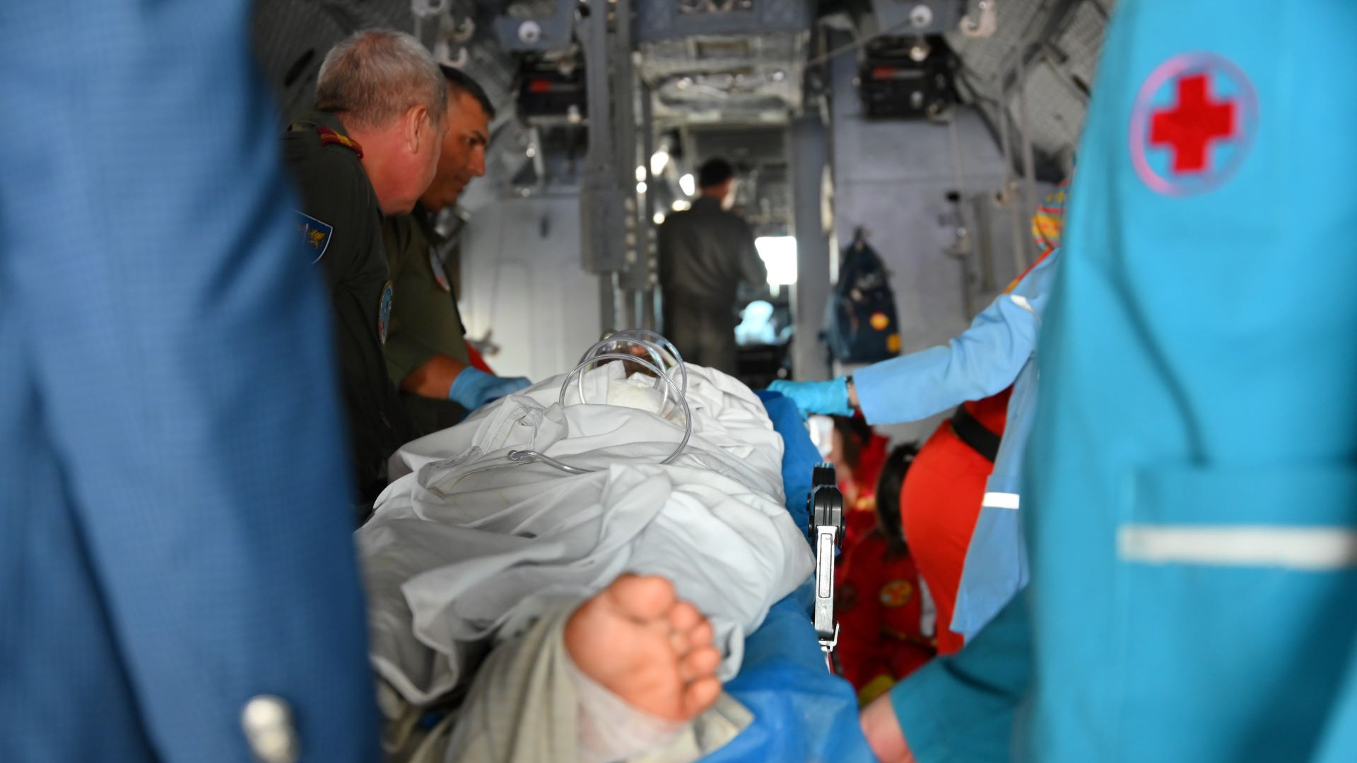 An injured person lies on a stretcher inside an ambulance, surrounded by paramedics providing urgent care