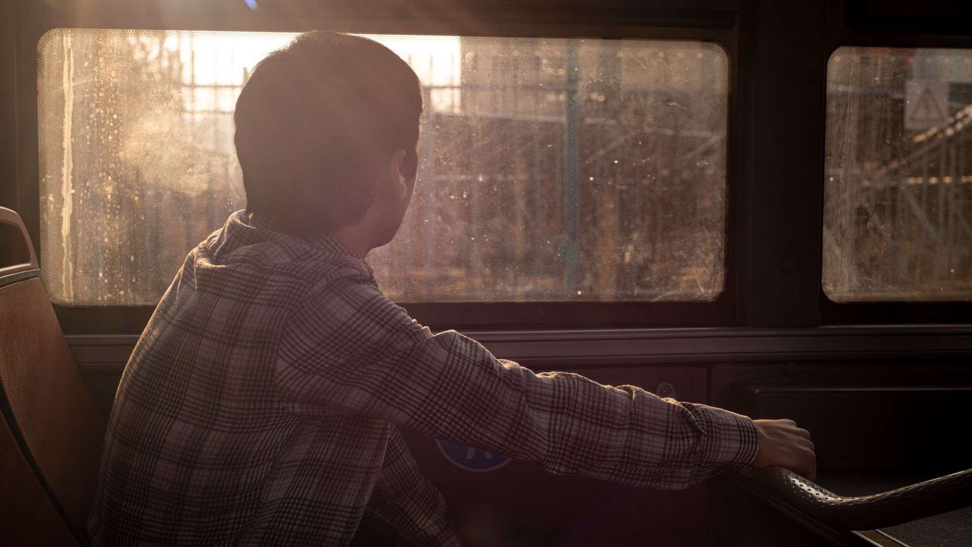 A person sits alone on a bus, looking out the window as sunlight streams in