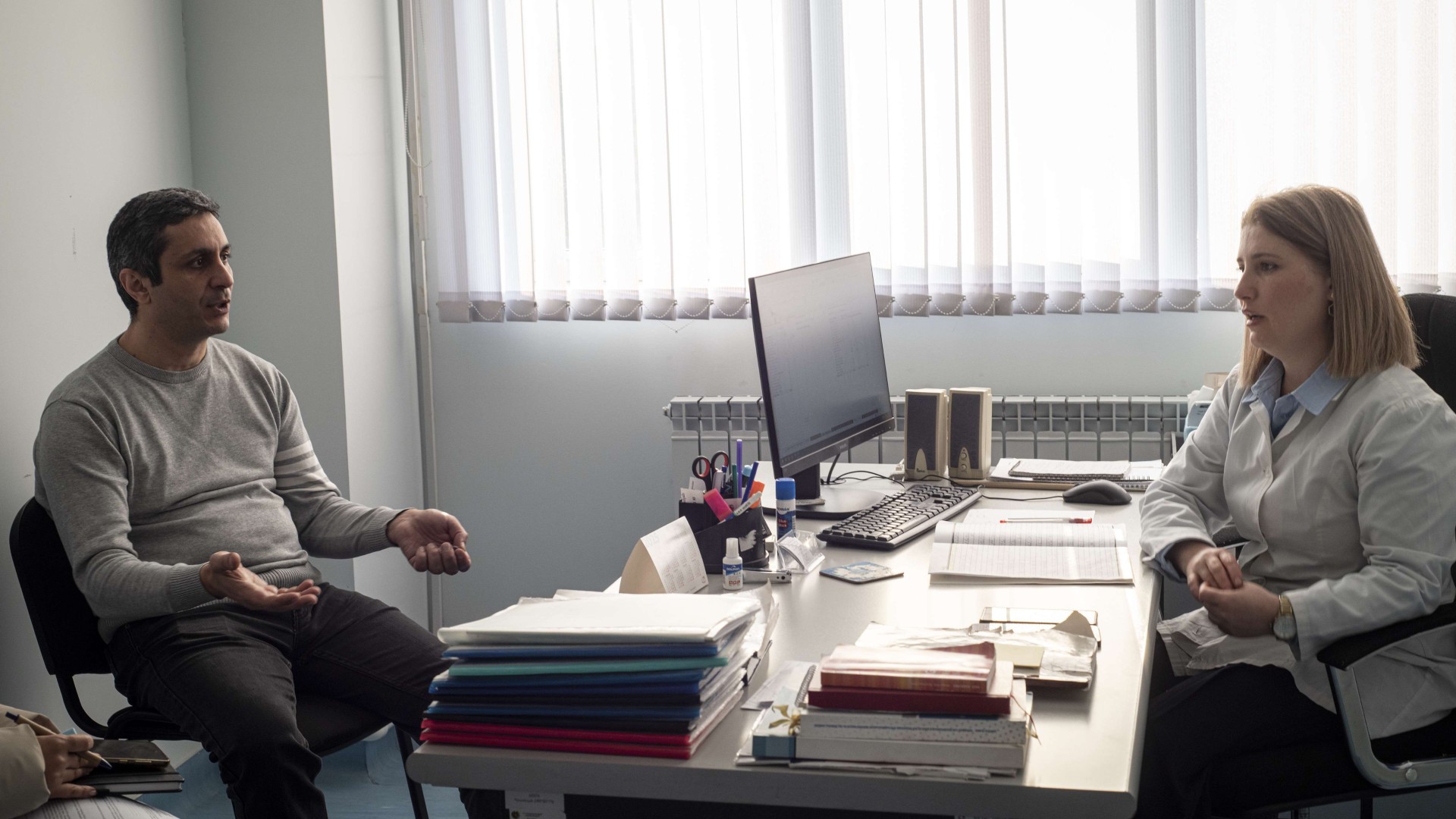 A man sits across from a healthcare professional in a bright, window-lit clinic room