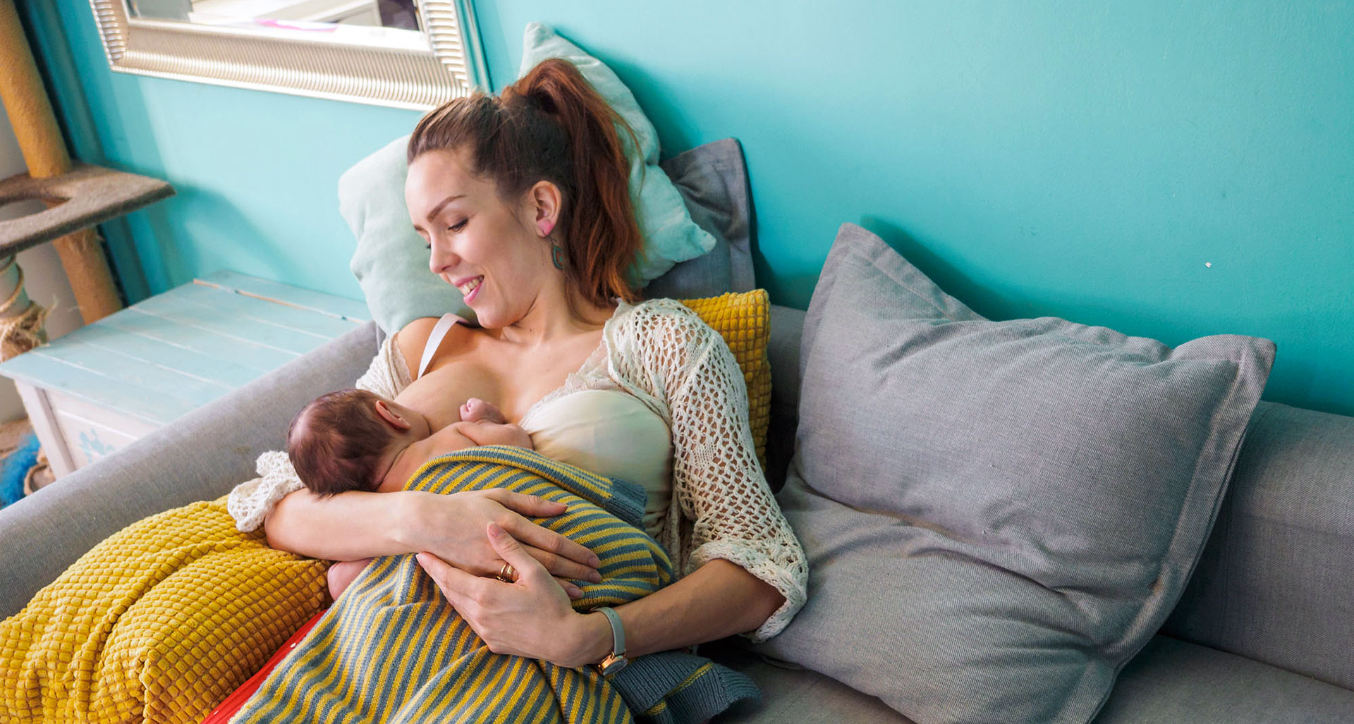 Smiling mother, breastfeeding her baby on a sofa.
