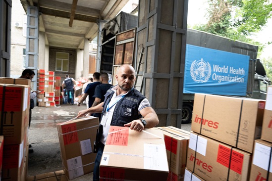 WHO and UNHCR workers loading supply boxes, for refugee and migrant health programmes.