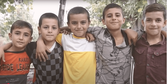 Five kids smile at the camera, their arms draped over each other's shoulders.
