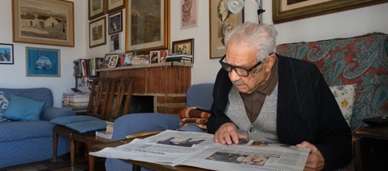 Older man with glasses carefully reads a newspaper in his living room